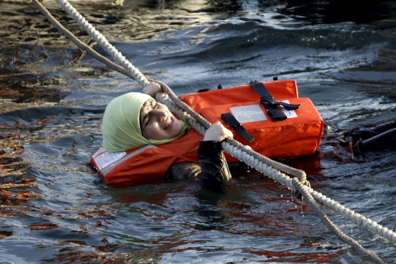 A refugee woman hangs on a rope as a half-sunken catamaran carrying around 150 refugees, most of them Syrians, arrives after crossing part of the Aegean sea from Turkey, on the Greek island of Lesbos