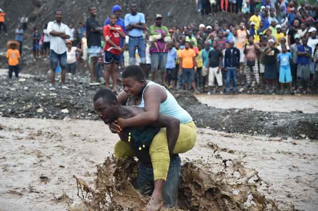 A man carries a woman across a  river at Petit Goave where a bridge collapsed during the rains of the Hurricane Matthew, southwest of Port-au-Prince, October 5, 2016.  Haiti and the eastern tip of Cuba -- blasted by Matthew on October 4, 2016 -- began the messy and probably grim task of assessing the storm's toll. Matthew hit them as a Category Four hurricane but has since been downgraded to three, on a scale of five, by the US National Hurricane Center. / AFP PHOTO / HECTOR RETAMAL